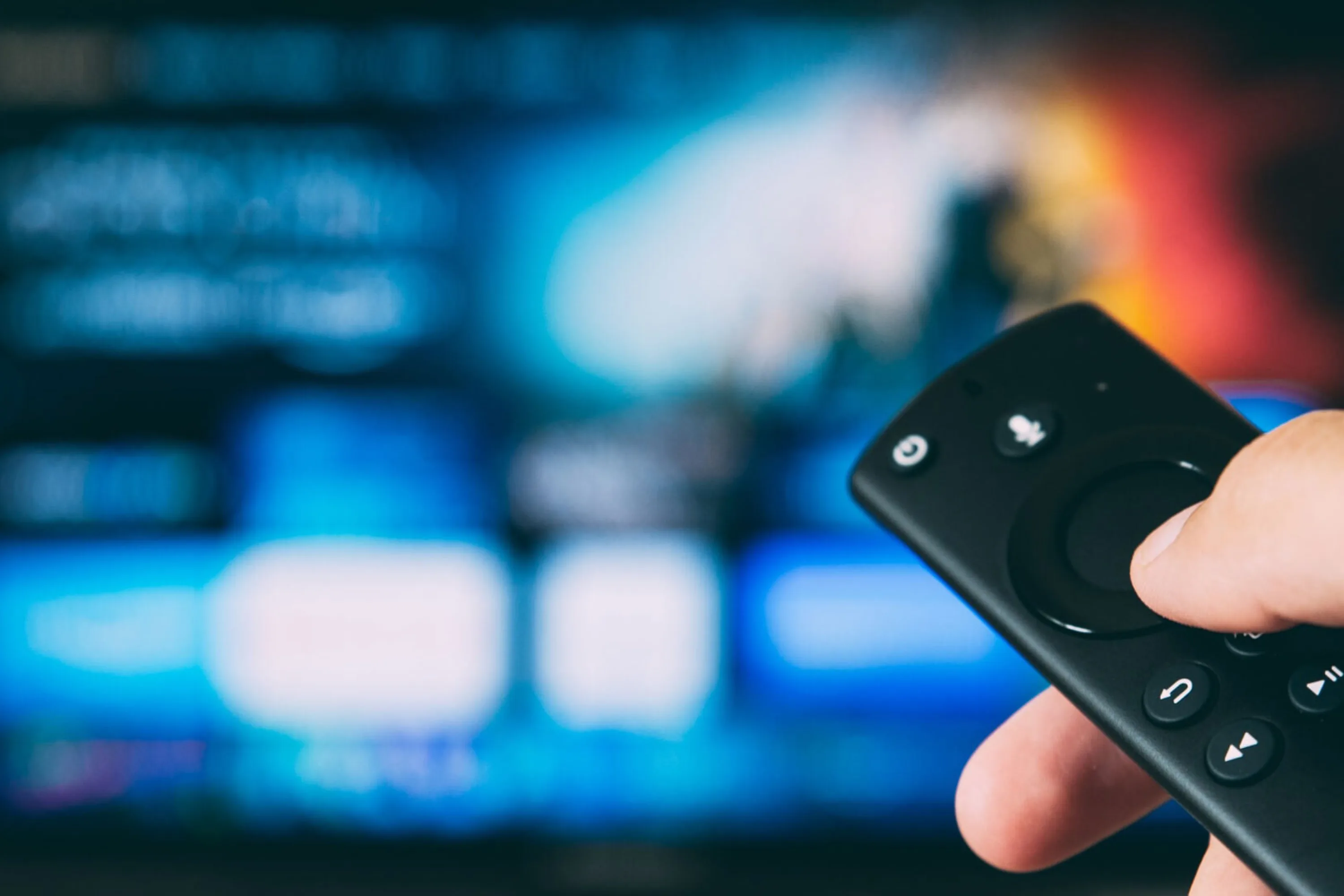 Hand holding a remote control with a blurred video on demand user interface in the background
