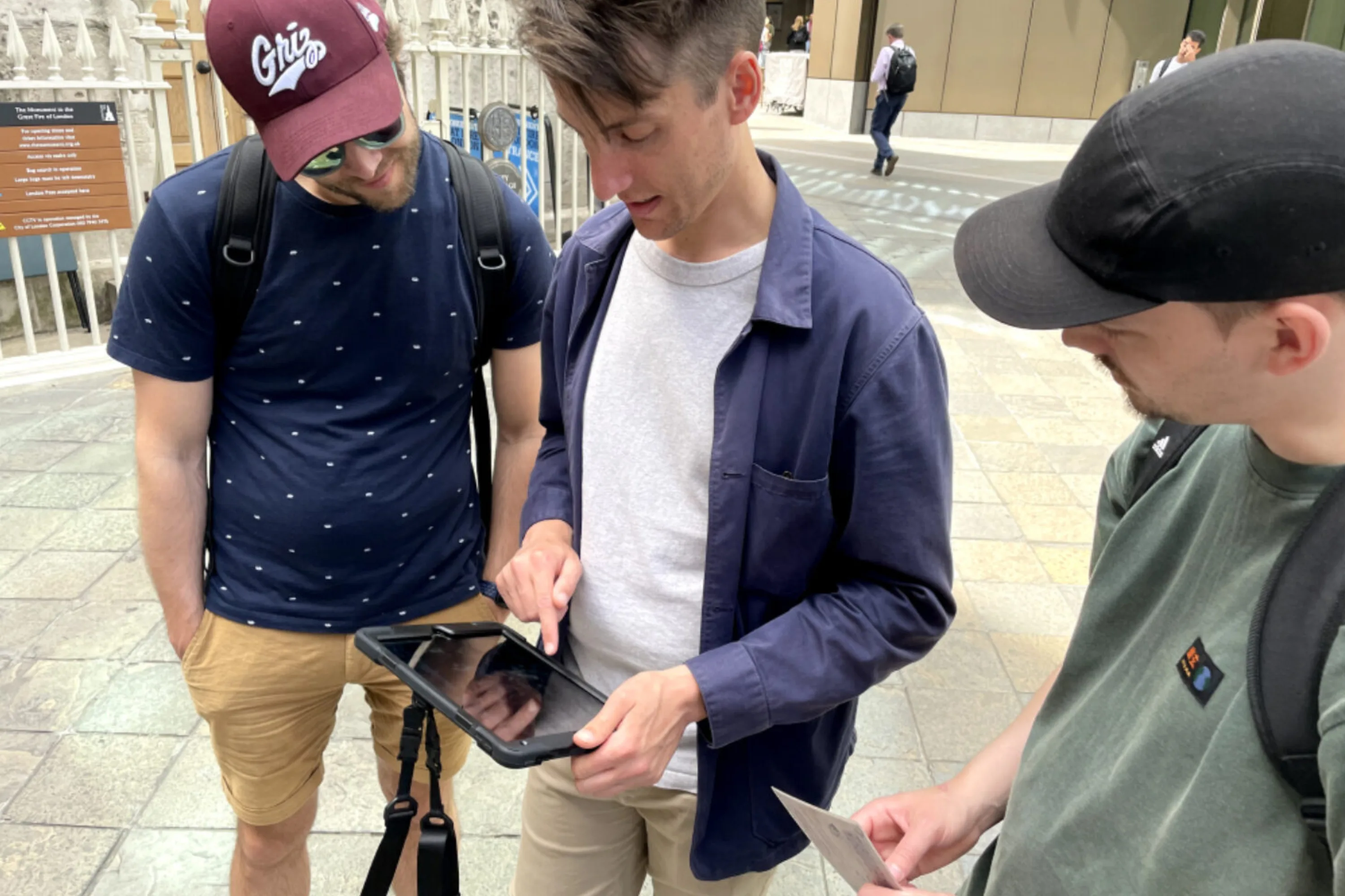 Three men look at an ipad in a city street