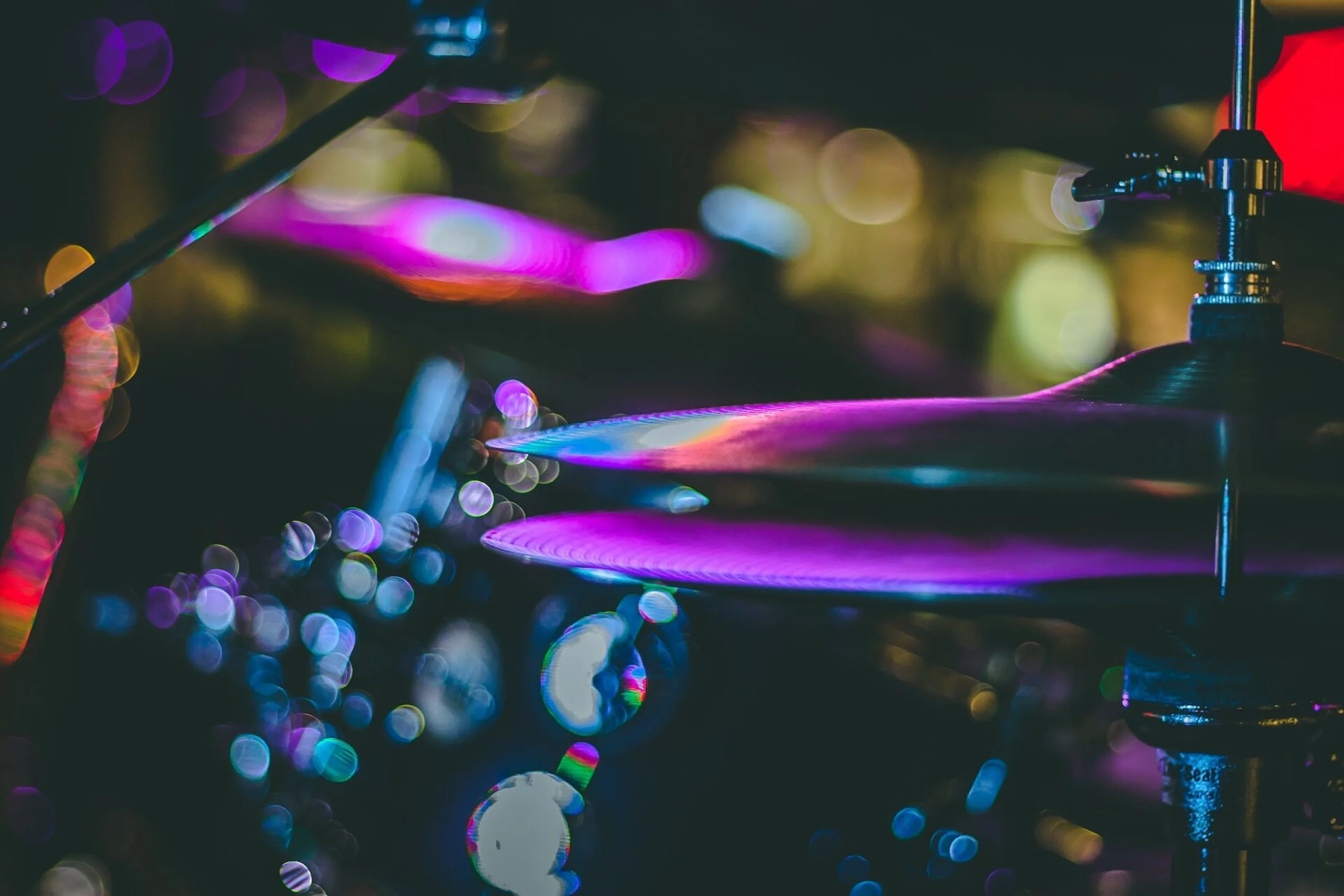 A photograph of cymbals reflecting purple light, in the low light of a jazz club.