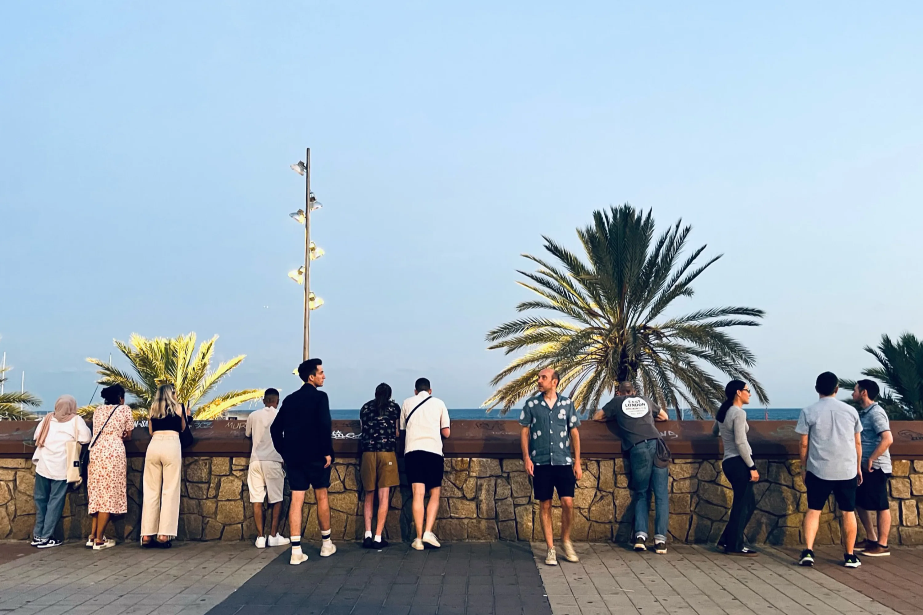 12 people look out at the sea under a clear sky
