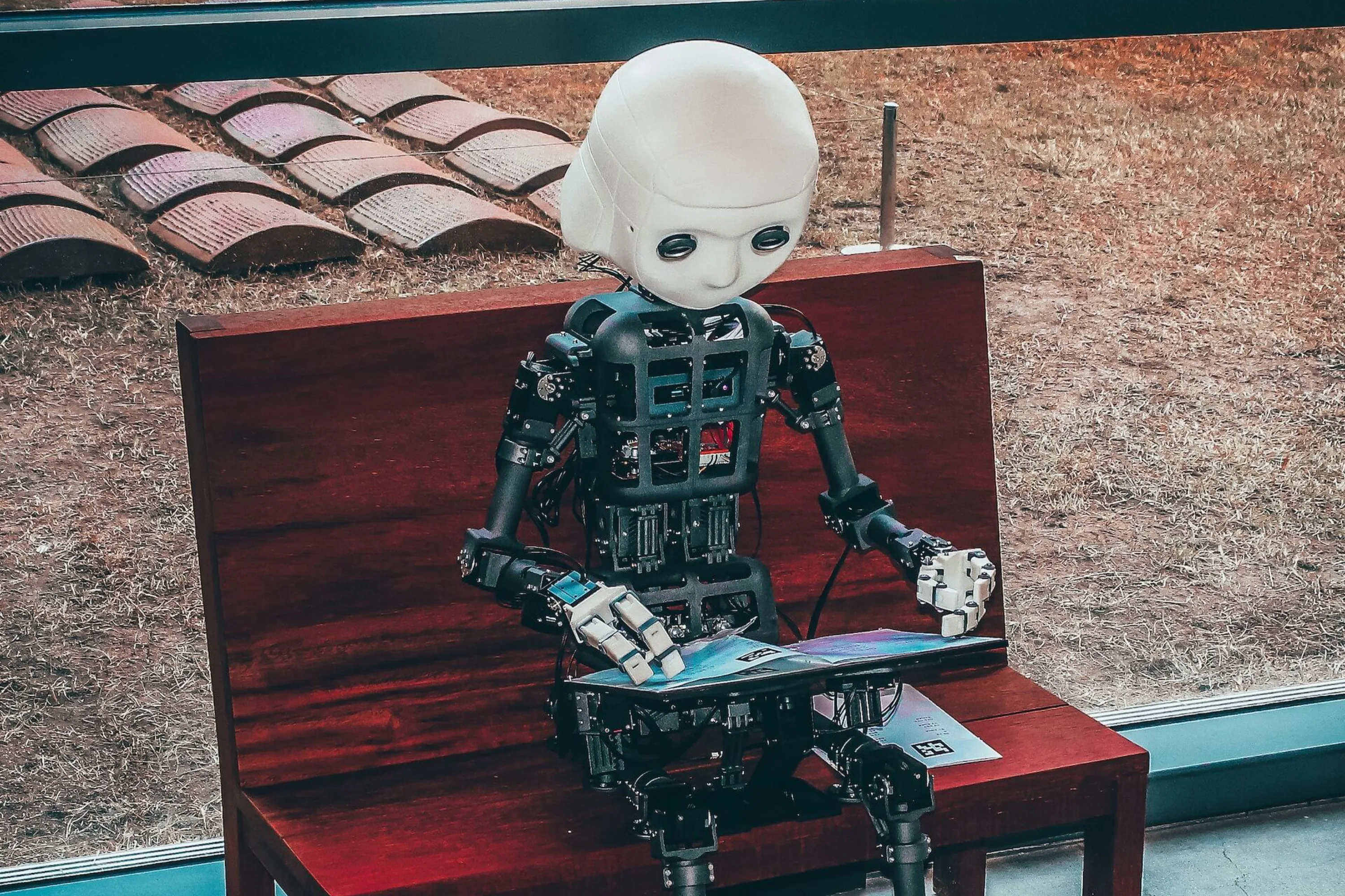 A robot sitting on a bench, reading a magazine.
