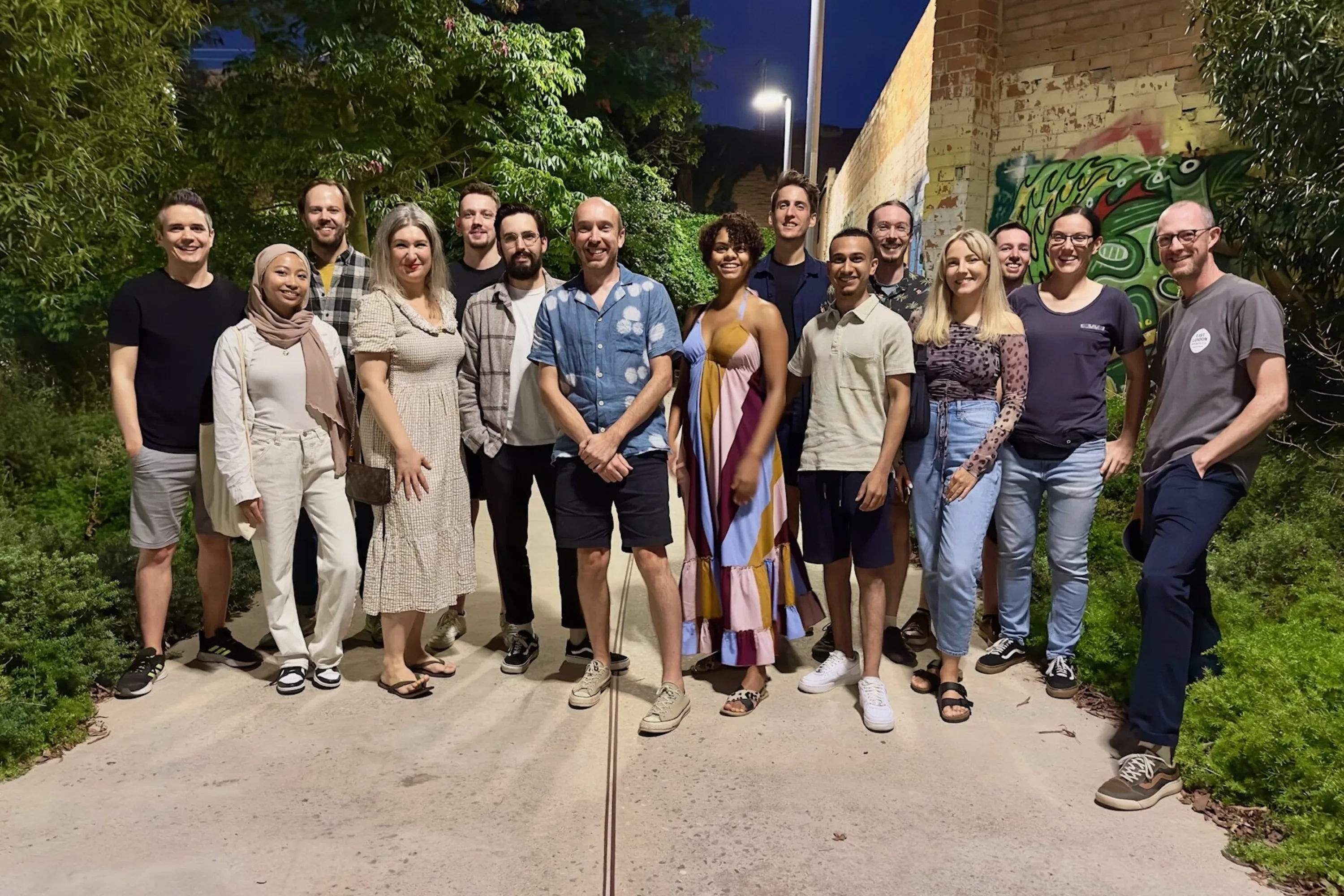 15 people pose for an informal team photo under street lights on a tree lines walkway