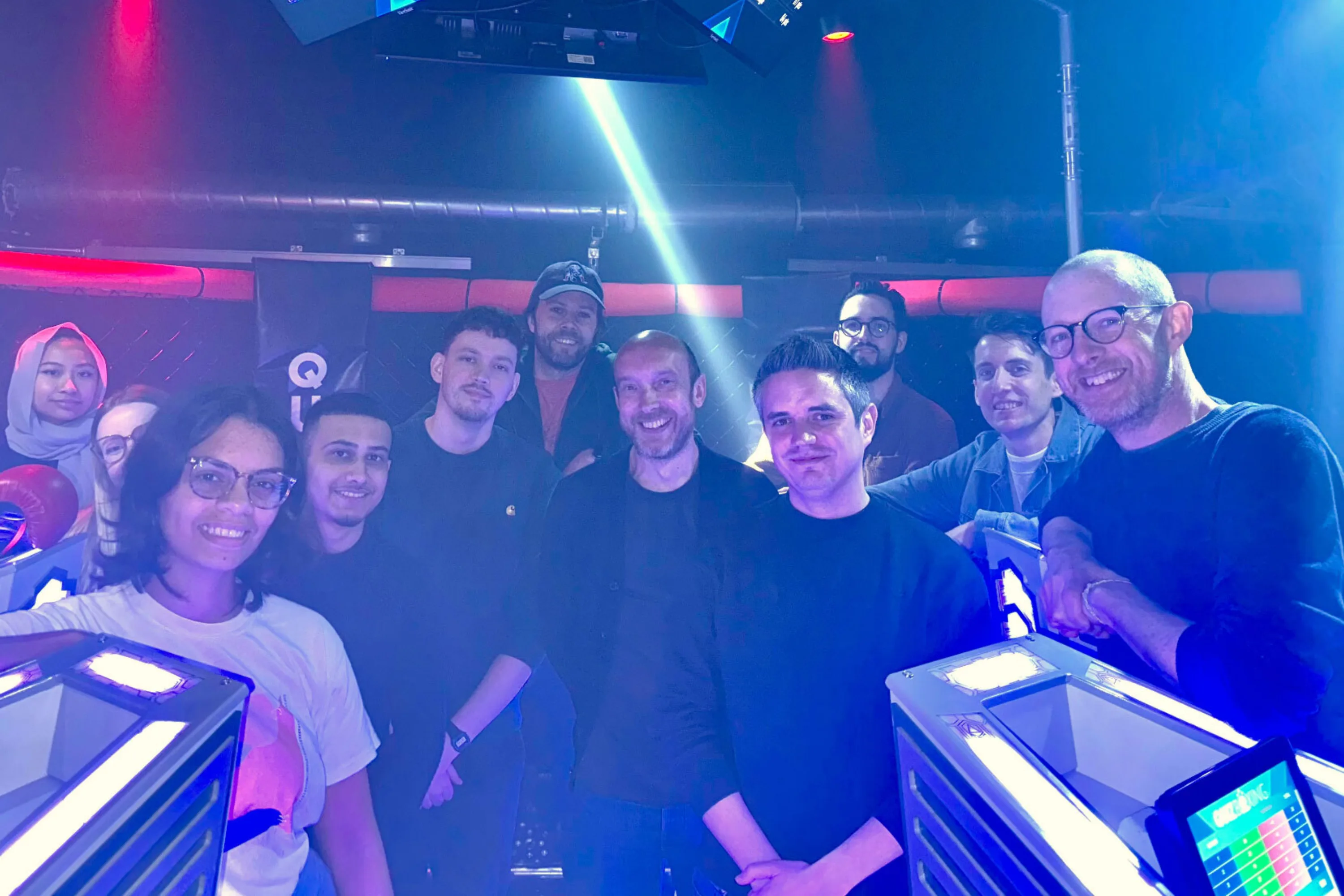 12 people pose for an informal photo in a room that looks like a TV quiz show set