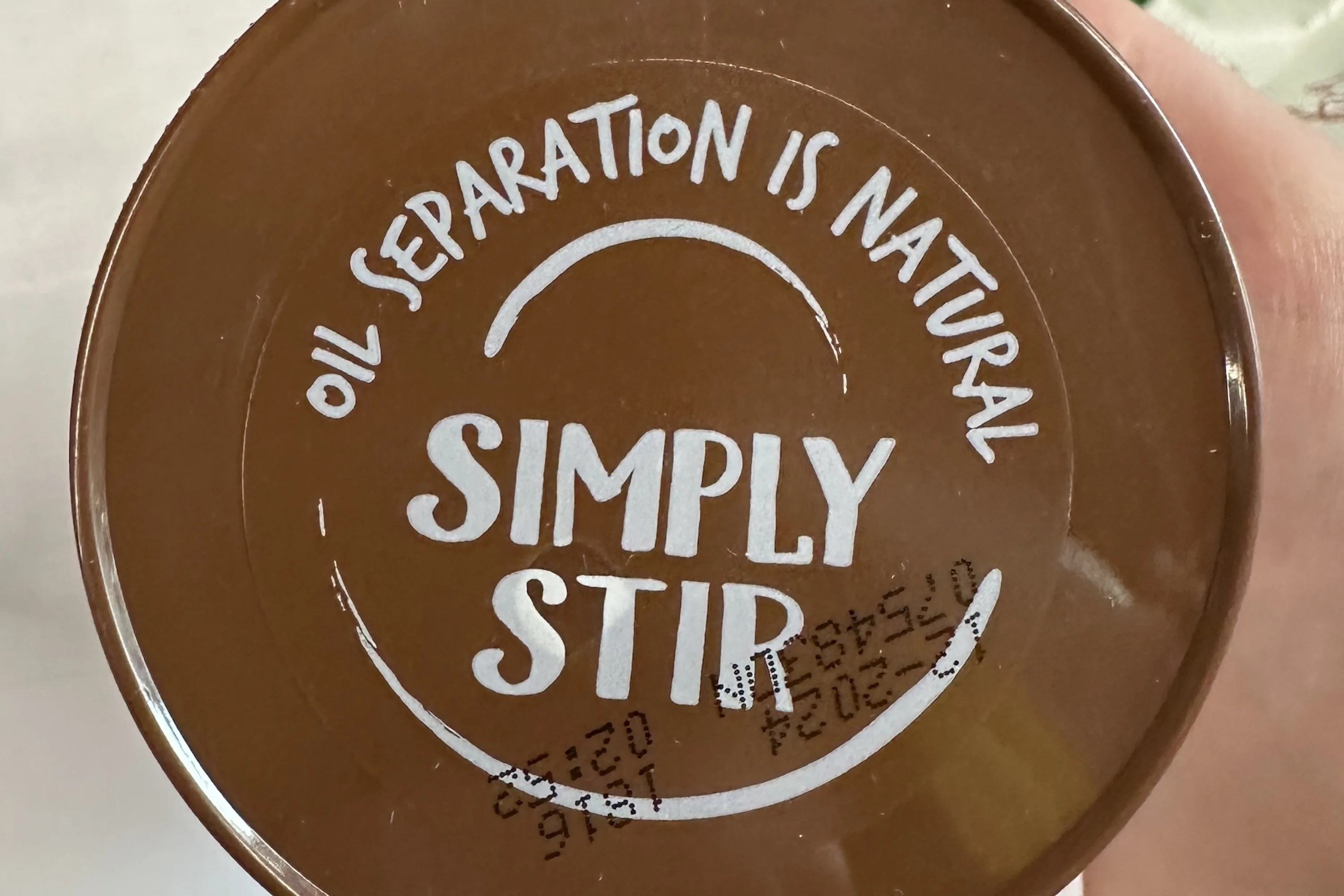 A brown lid from of a jar of peanut butter, with printed instructions to stir before use.
