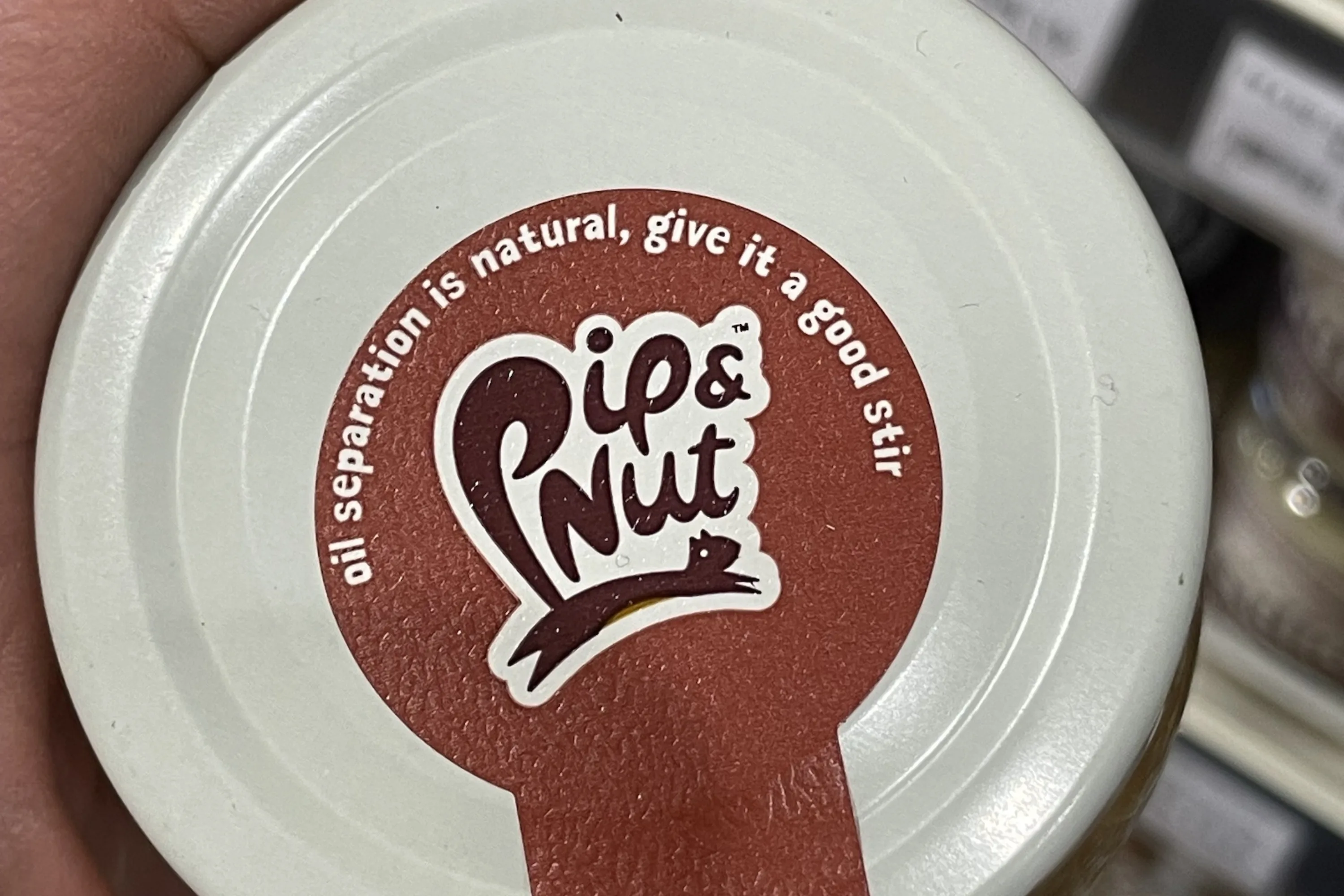 The lid of a jar of Pip & Nut brand peanut butter, with printed instructions to stir before use.
