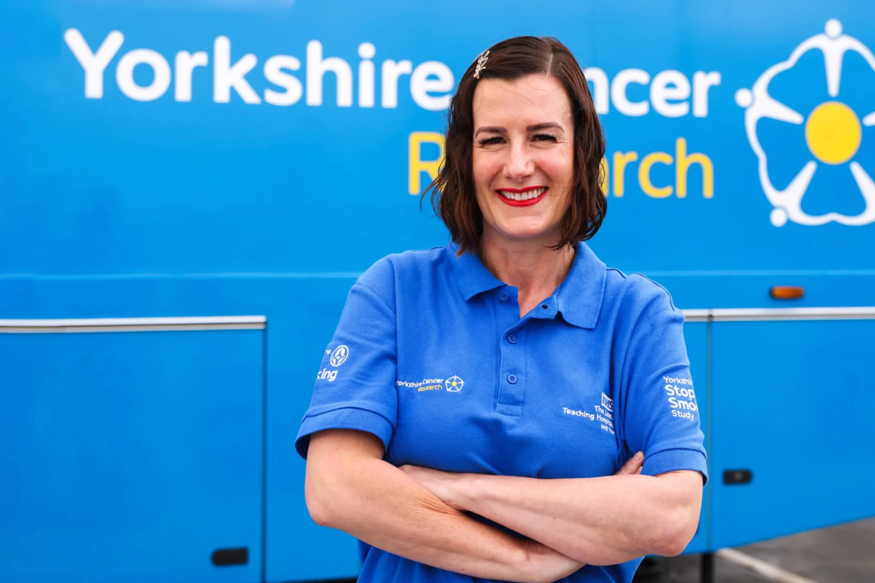 A woman in a Yorkshire Cancer research t-shirt standing proudly in front of a Yorkshire Cancer research bus