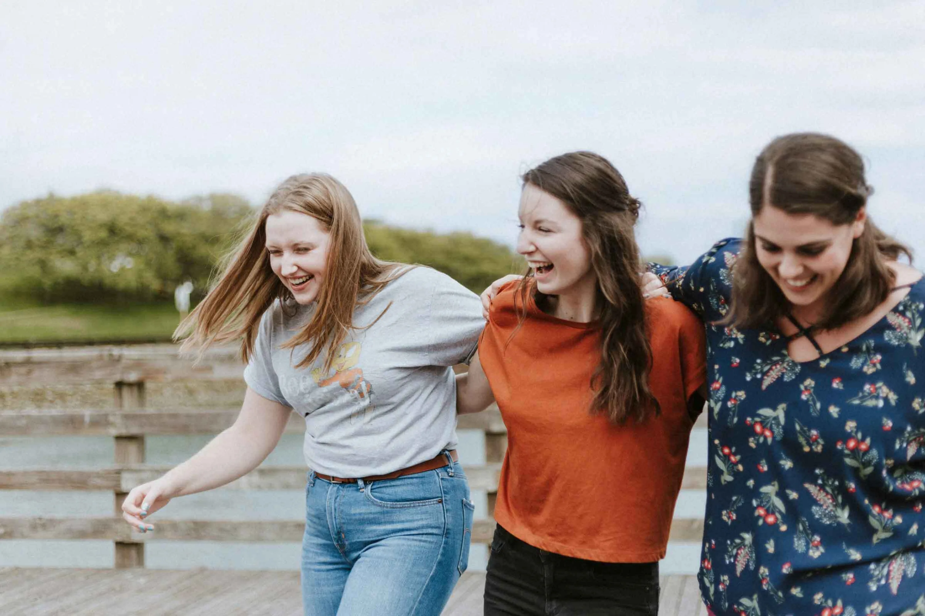 Three young women walk arm in arm on a broad walk by the water
