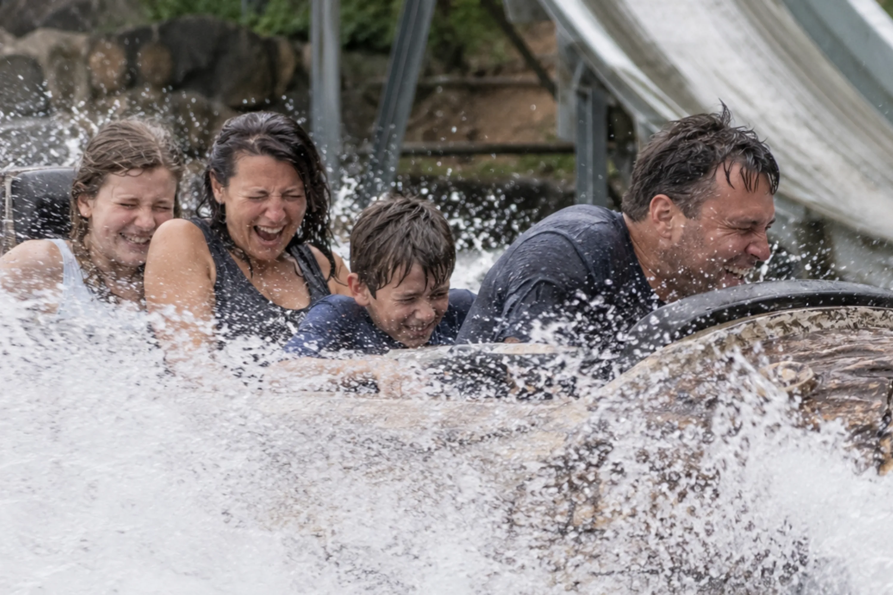 Four riders laugh and brace themselves as their log flume boat sends a wave of water splashing around them.