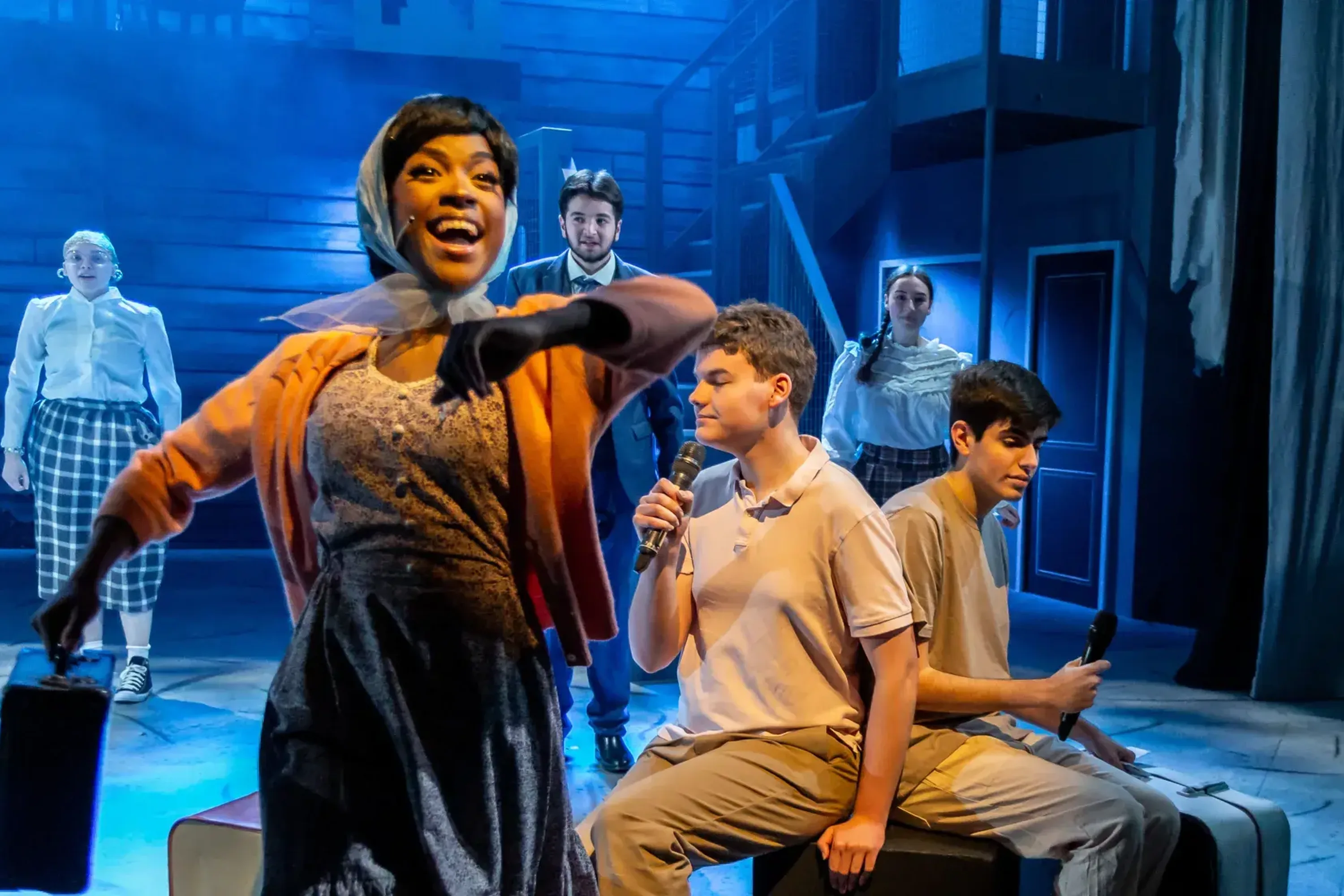 A black woman in period costume smiles widely on stage with 5 people behind her