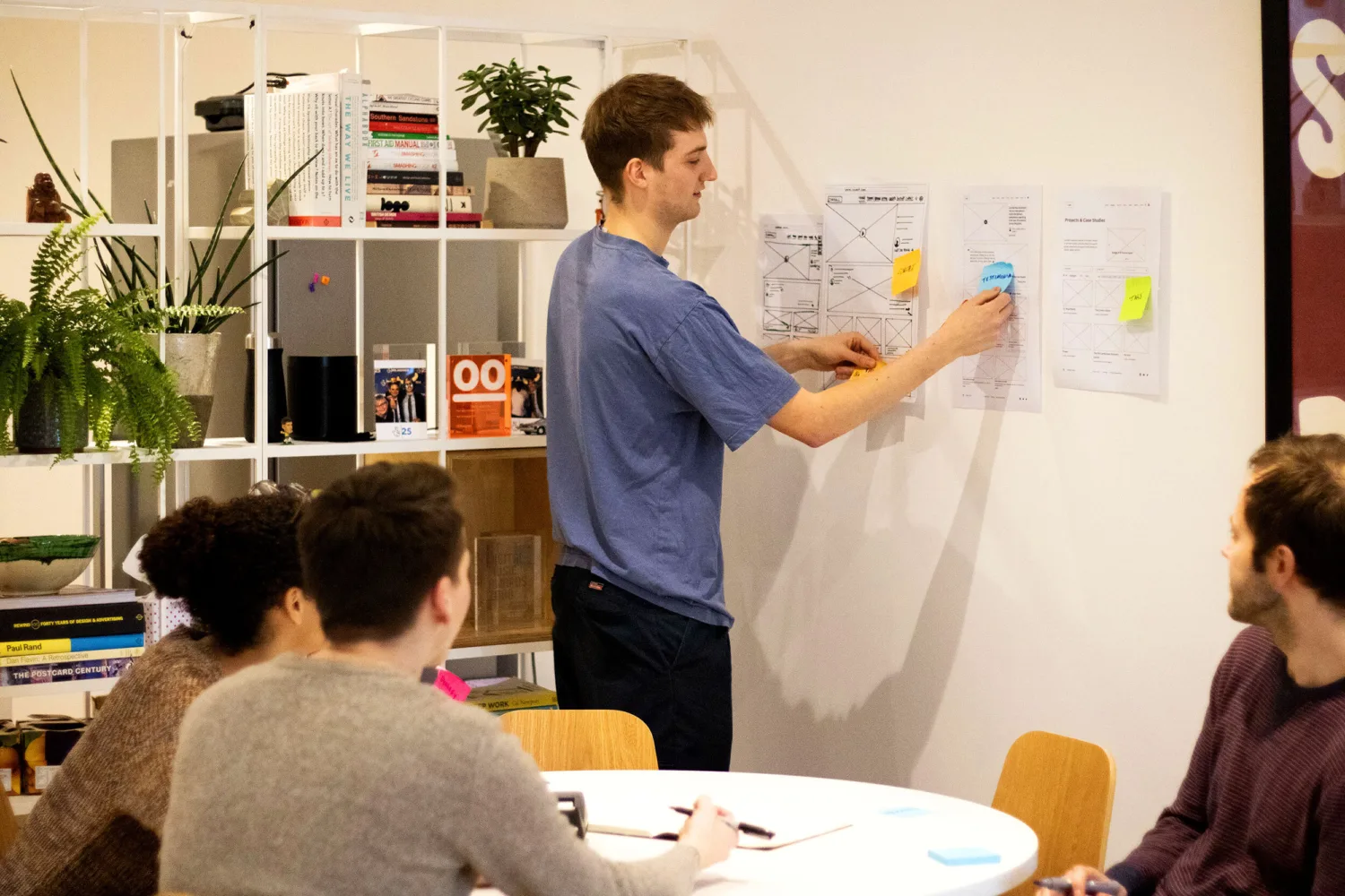 A team of web designers discuss wireframe designs by pinning them to the wall