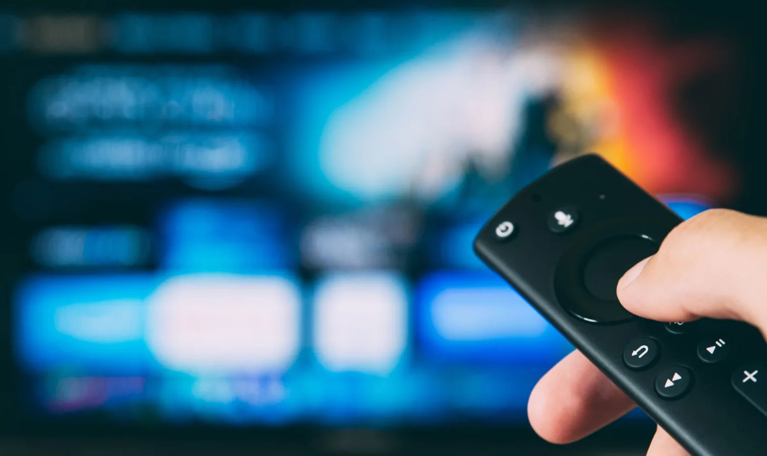 Hand holding a remote control with a blurred video on demand user interface in the background