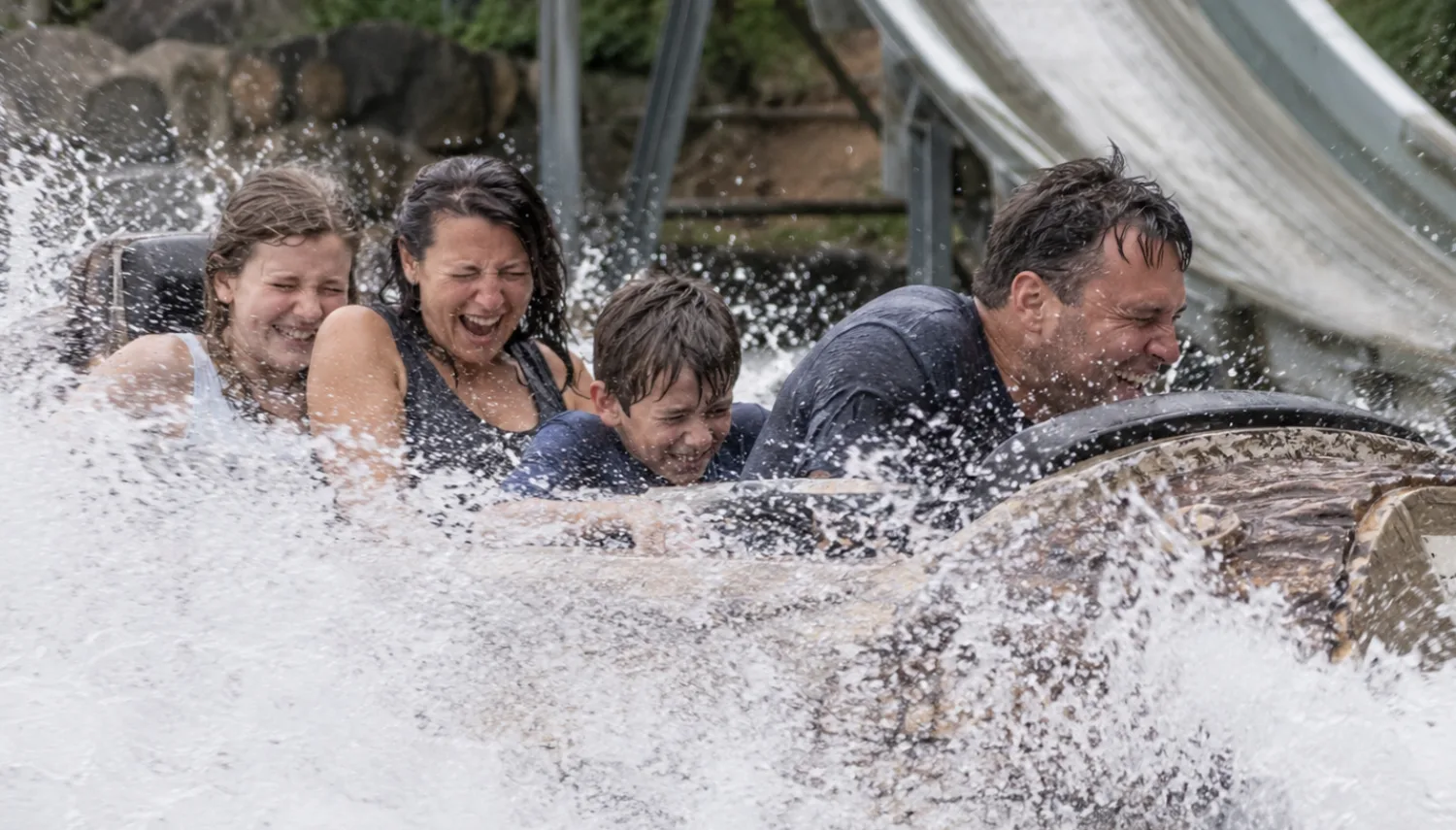 Four riders laugh and brace themselves as their log flume boat sends a wave of water splashing around them.