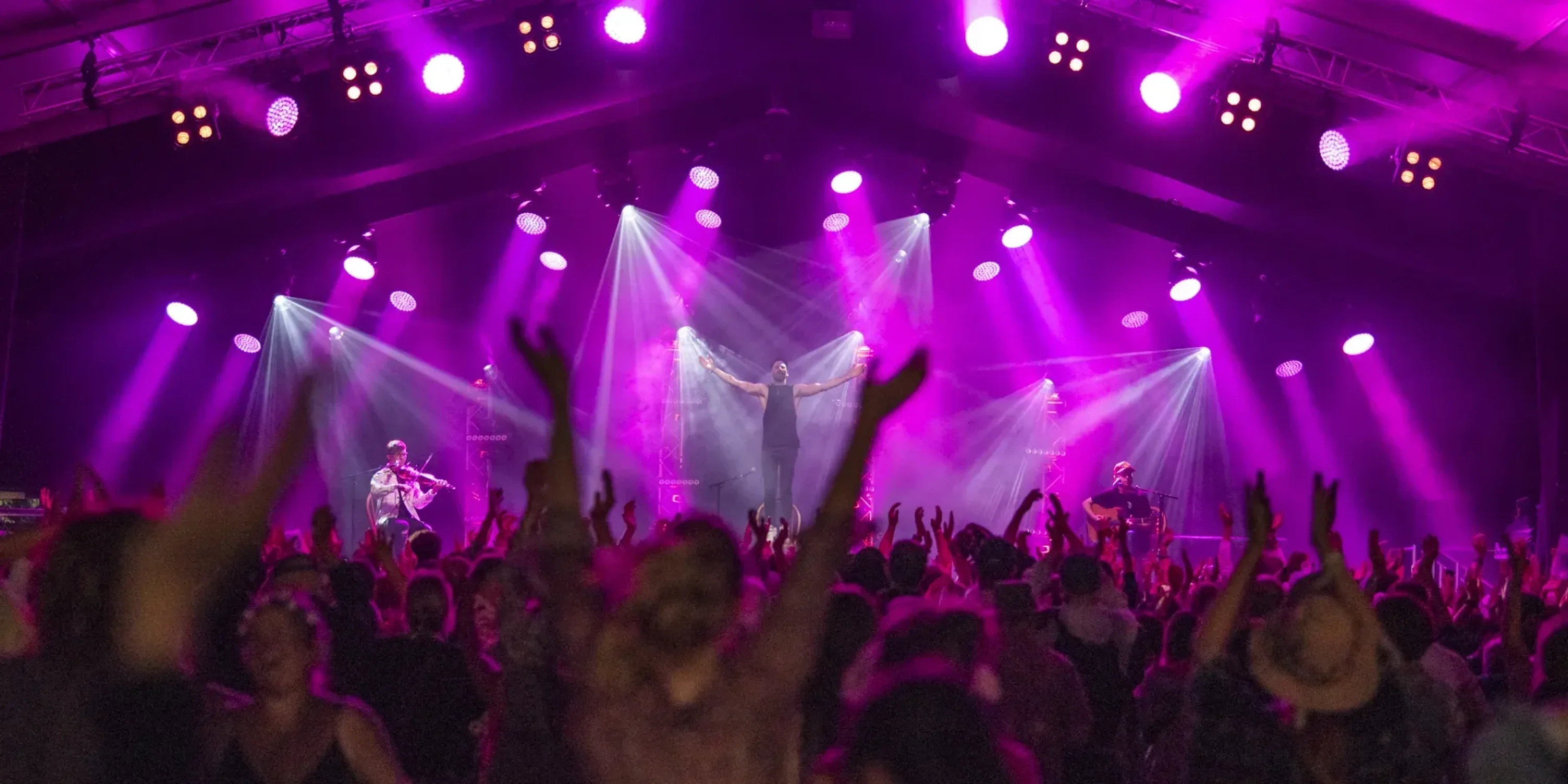 A man stands on a concert stage in front of a cheering audience