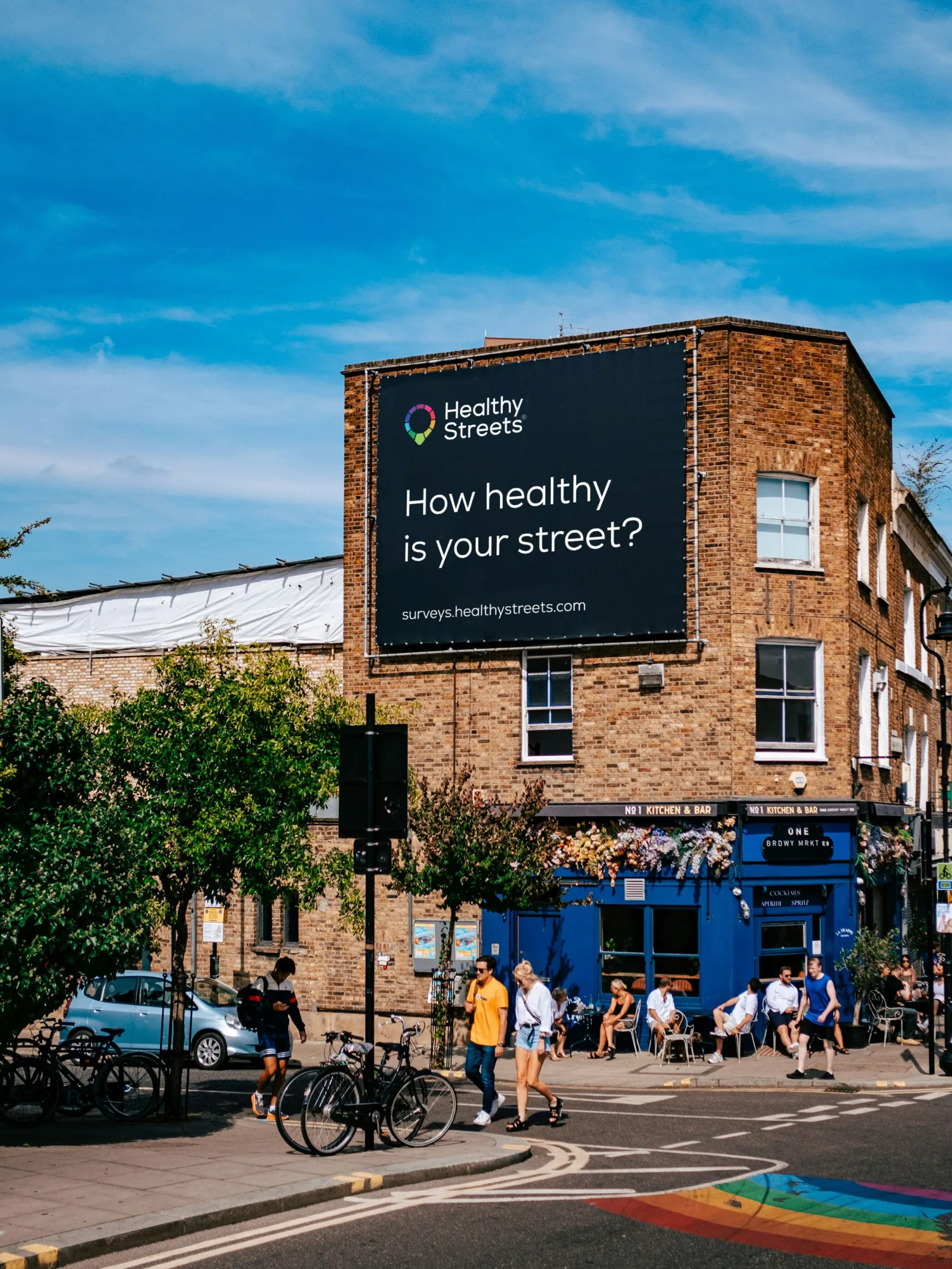 Street corner in summer with a large poster: How healthy is your street?