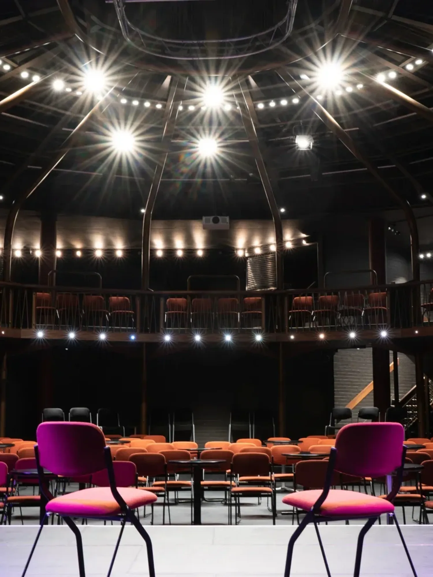 Two chairs sit on a stage facing a dark auditorium and bright theatre lighting