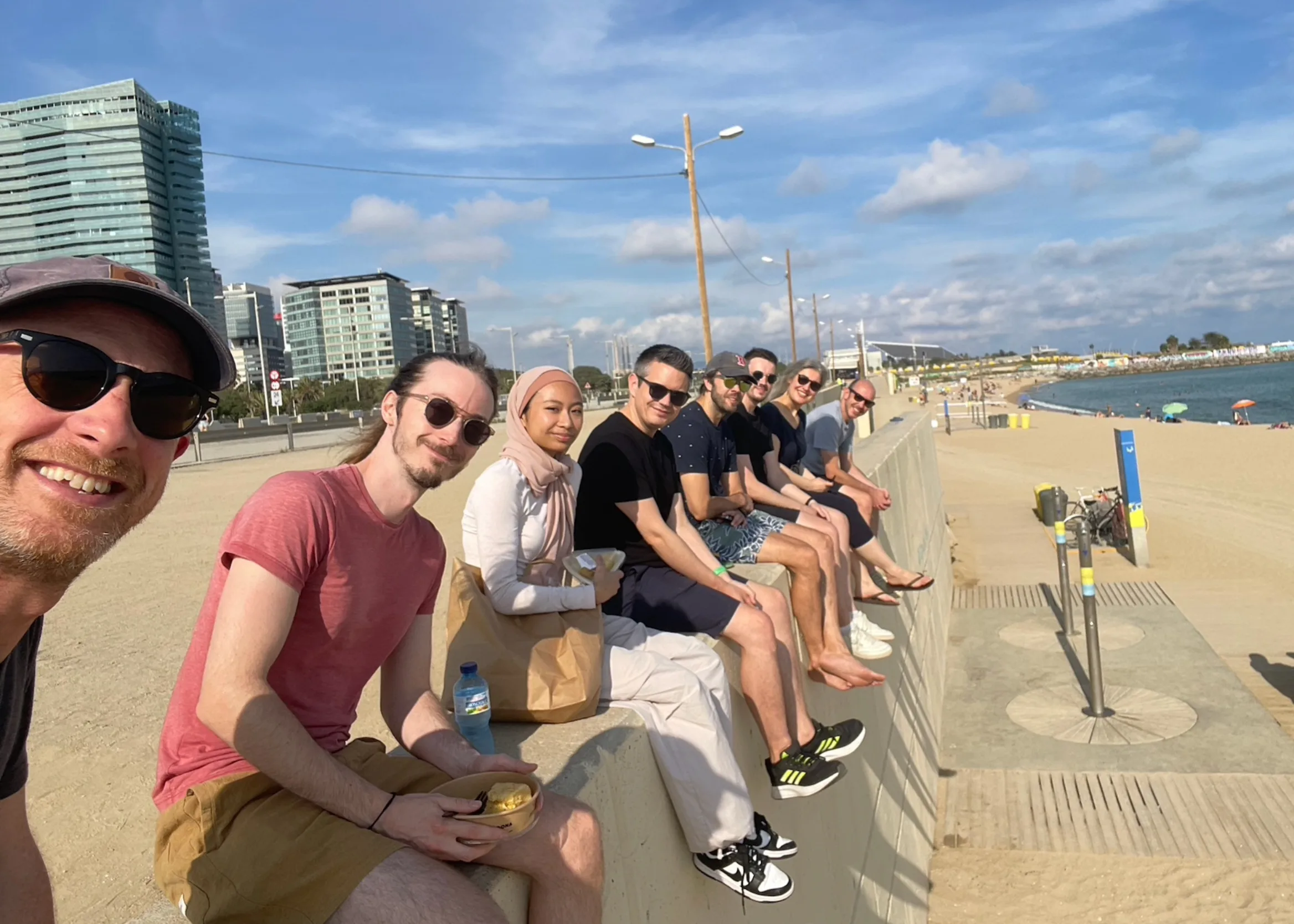 A number of people sit on a wall above a beach