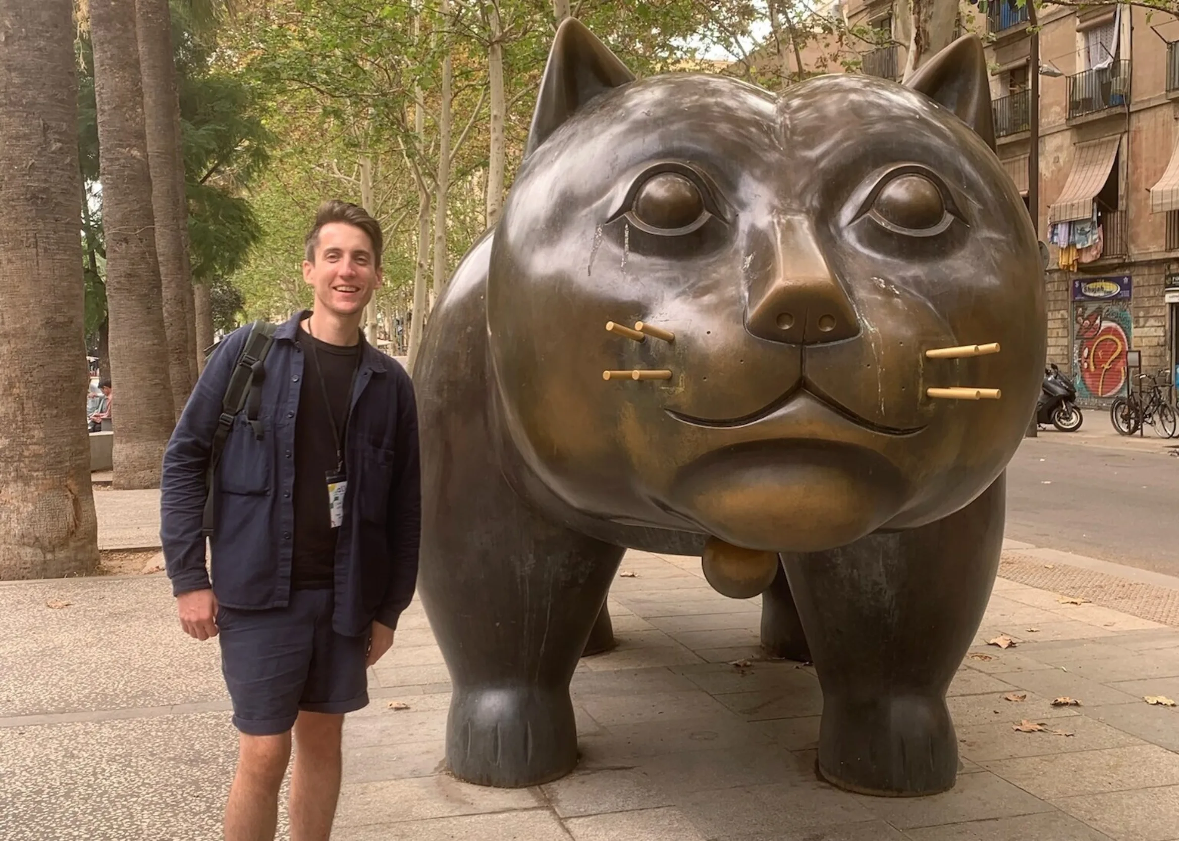 A man standing next to an enormous brass cat sculpture
