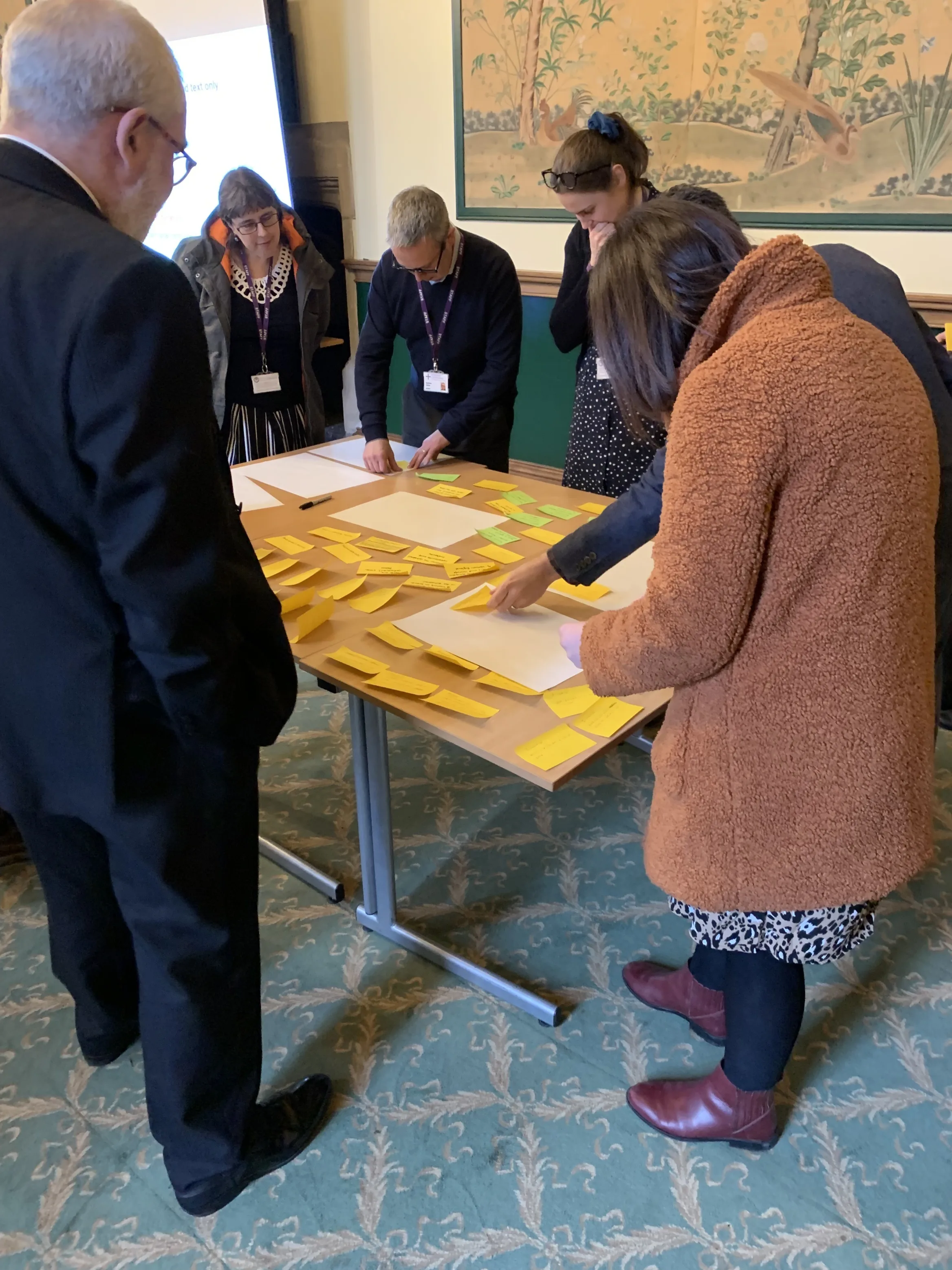 People standing around a central table placing post-it notes on larger pieces of paper