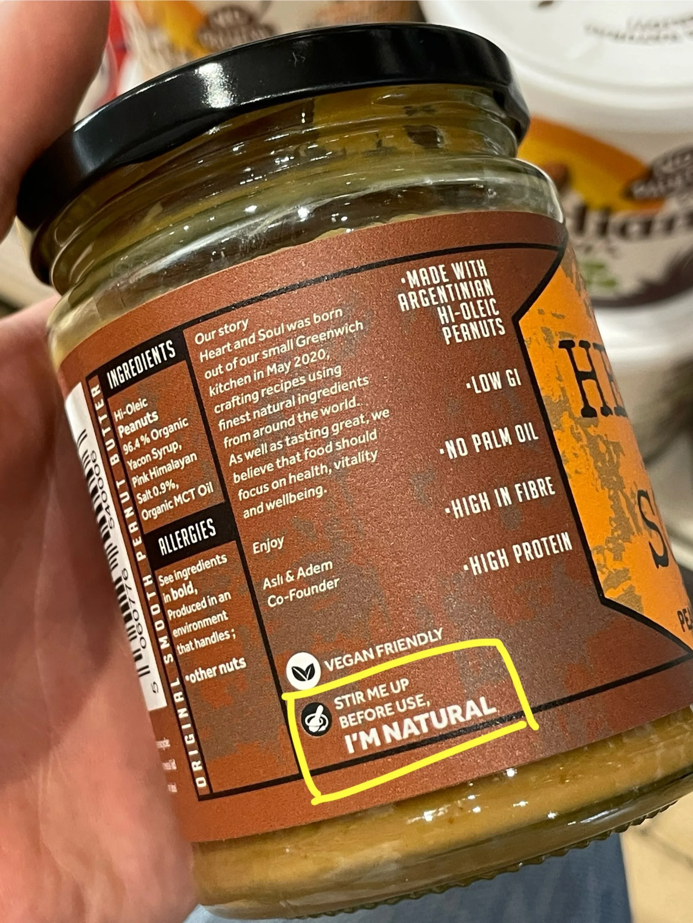 Side of a peanut butter jar with writing showing ingredients, allergy info, "our story", vegan friendly label and, eventtually, a message about stirring before use.