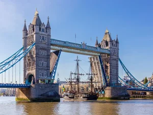 A tall sail ship passes through the raised bascules of Tower Bridge