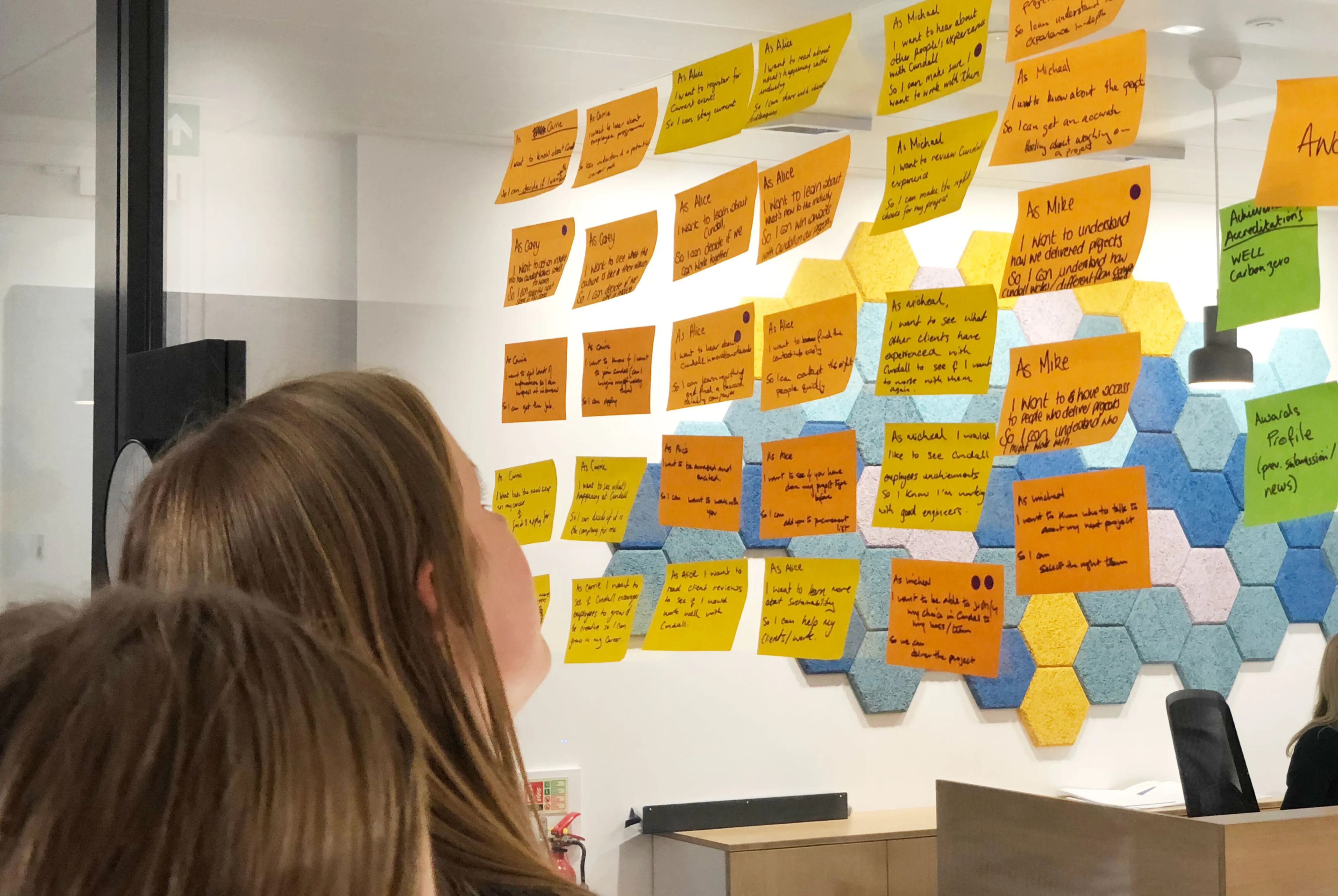 Women assess user stories on post-it notes pasted to a glass wall